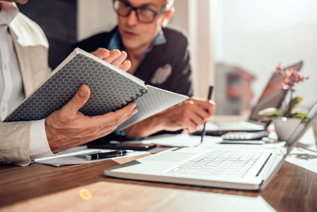 Zwei Herren mit Laptops und Notizbuch am Tisch, 24-Stunden-Pflege