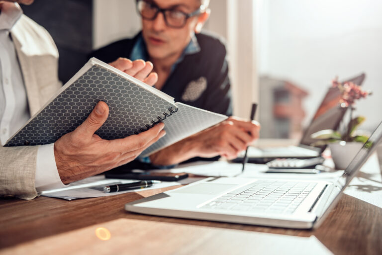 Zwei Herren mit Laptops und Notizbuch am Tisch, 24-Stunden-Pflege