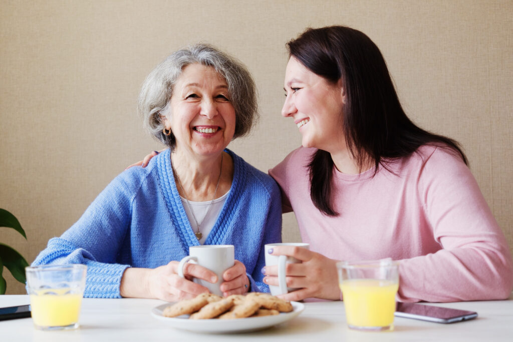 Betreuungskraft mit älterer Dame am Tisch mit Kaffee, 24-Stunden-Pflege