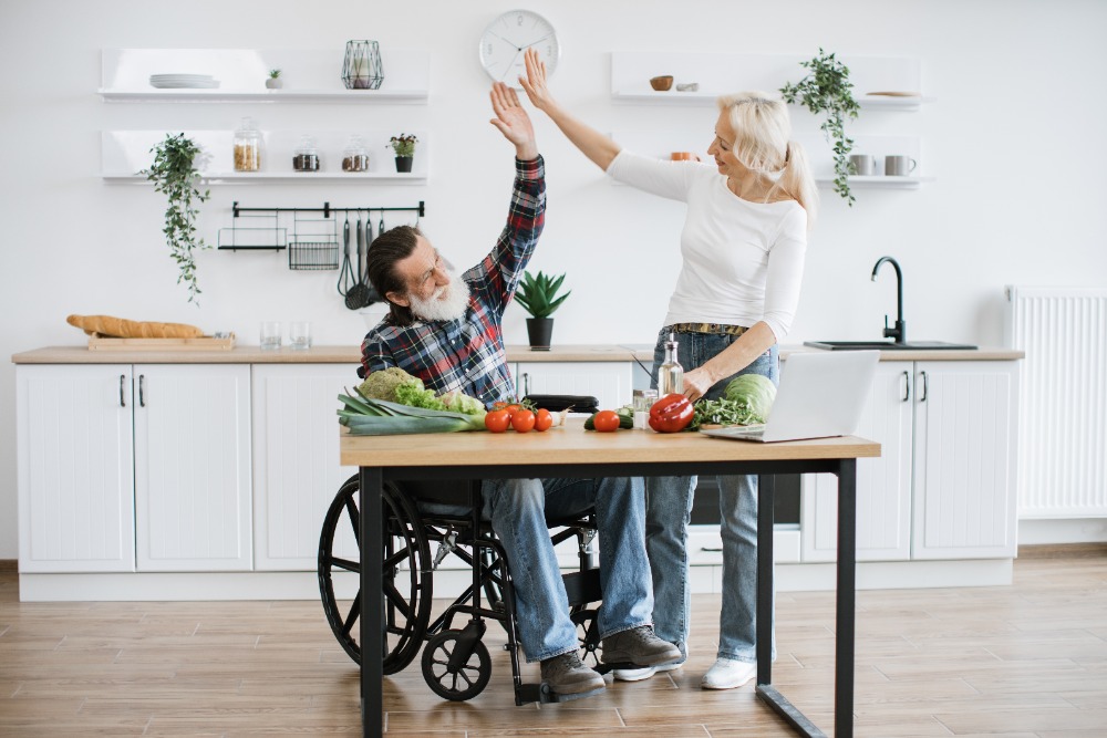 Herr im Rollstuhl gibt seiner Betreuungskraft ein High Five während der 24-Stunden-Pflege und Mahlzeitenvorbereitung