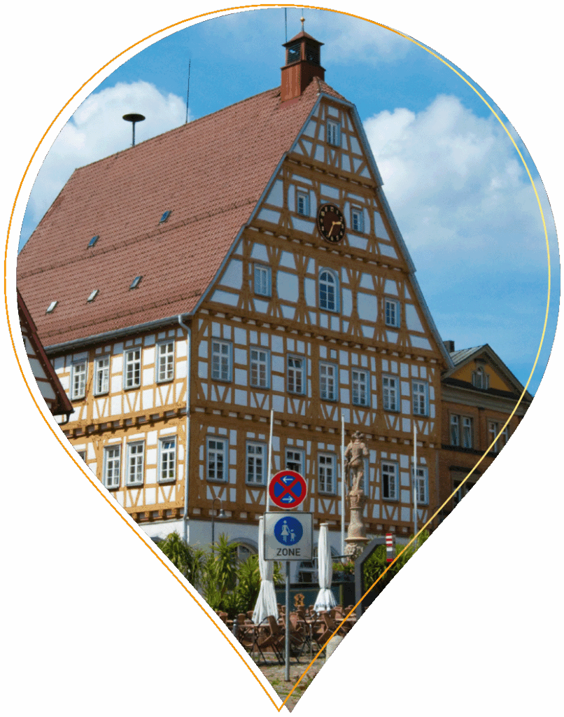 Ein traditionelles deutsches Fachwerkhaus in Leonberg mit steilem rotem Dach und einer Uhr an der Fassade, die sich hinter Straßenschildern und Straßencafés unter blauem Himmel verbirgt.