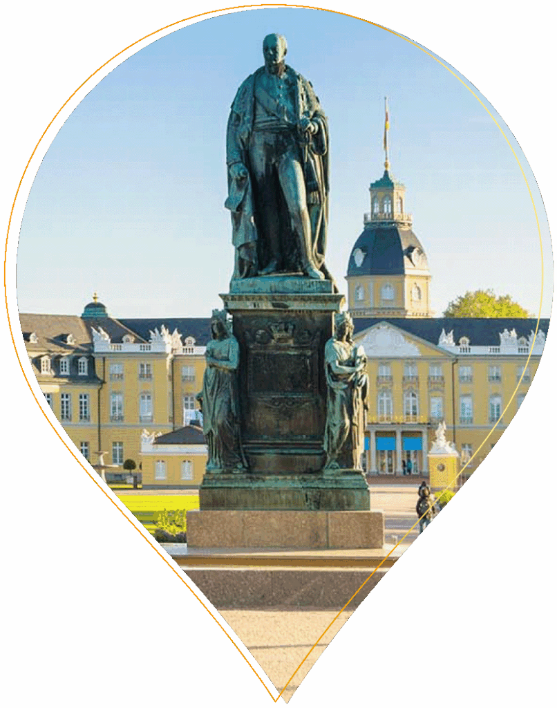 Eine Bronzestatue steht vor einem großen gelben Palast mit Kuppeldach und einer Fahne auf dem Dach, unter einem klaren blauen Himmel, umrahmt von einer nadelförmigen Umrandung.