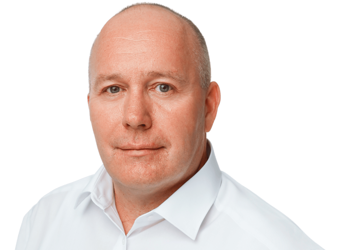 Matthias Koepke, ein Mann mittleren Alters mit rasiertem Kopf und weißem Kragenhemd blickt mit neutralem Gesichtsausdruck direkt in die Kamera vor einem schlichten Hintergrund.