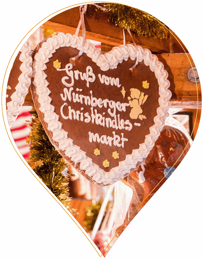 Ein herzförmiger Lebkuchen, verziert mit weißem Zuckerguss und dem Schriftzug Gruß vom Nürnberger Christkindlesmarkt, hängt an einem festlichen Marktstand.