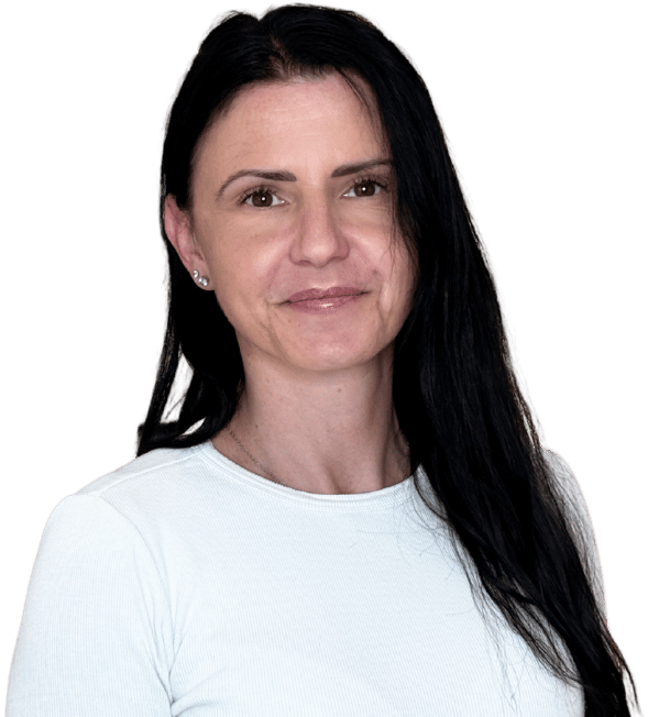 Sanela Gerzic - Eine Frau mit langen dunklen Haaren, die ein helles langärmeliges Hemd trägt, steht vor einem transparenten Hintergrund und lächelt sanft in die Kamera.