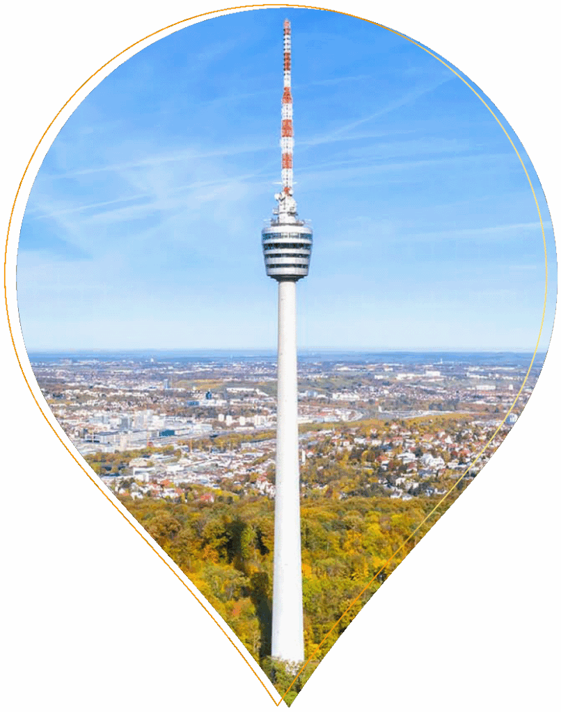 Der Fernsehturm in Stuttgart mit einer rot-weißen Antenne steht über einer Stadtlandschaft, umgeben von Bäumen und Gebäuden unter einem blauen Himmel, eingerahmt von einem kartennadelförmigen Rahmen.