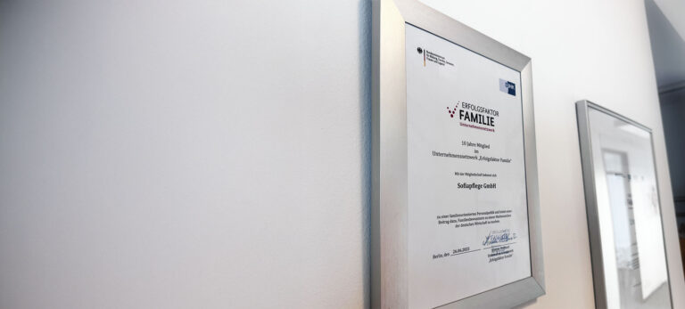 Eine gerahmte Urkunde mit dem Titel "Erfolgsfaktor Familie" hängt an einer weißen Wand und reflektiert das Licht. Diese deutsche Auszeichnung, die von offiziellen Organisationen vergeben wird, unterstreicht die Bedeutung der Familie als Schlüsselfaktor für den Erfolg.