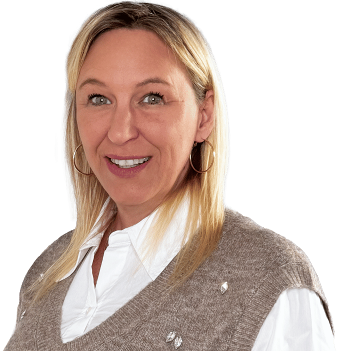 Jasmine Dinies, eine Frau mit glattem blondem Haar, die Ohrringe, ein weißes Hemd mit Kragen und eine hellbraune Pulloverweste trägt, lächelt in die Kamera vor einem schlichten weißen Hintergrund.