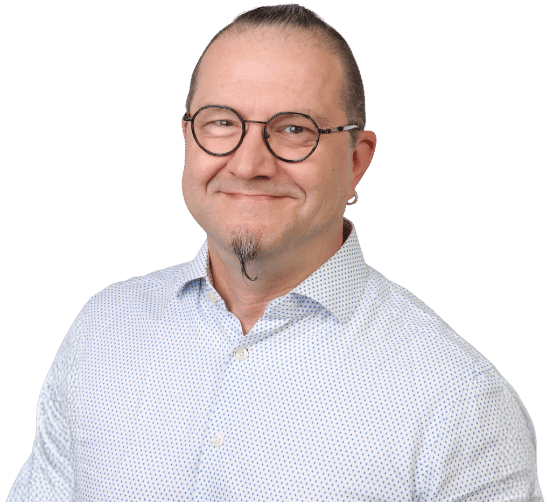 Matthias Wöhr, ein lächelnder Mann mit Brille, kurzem Bart und kleinem Spitzbart, trägt ein hellblau gemustertes Button-up-Hemd und steht vor einem schlichten weißen Hintergrund.
