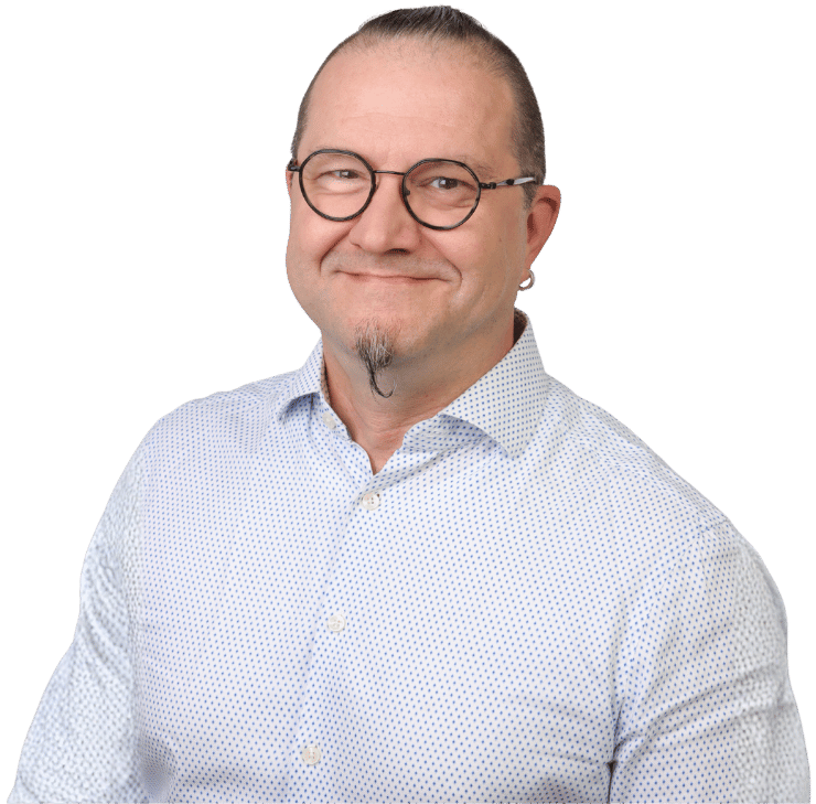 Matthias Wöhr, ein lächelnder Mann mit kurzem, geglättetem Haar, Brille, Spitzbart und Ohrring, trägt ein hellblau gemustertes Button-up-Hemd, während er vor einem schlichten weißen Hintergrund posiert.