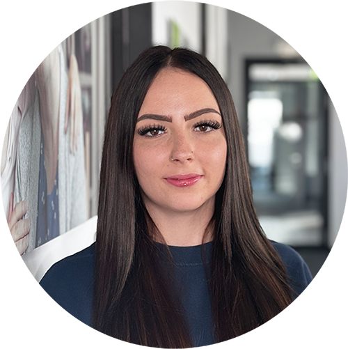 Patricia Wildermuth, eine Frau mit langen glatten dunklen Haaren und einem marineblauen Oberteil, steht in einem Haus und schaut in die Kamera. Der Hintergrund ist unscharf und zeigt einen Flur und gerahmte Bilder an der Wand.