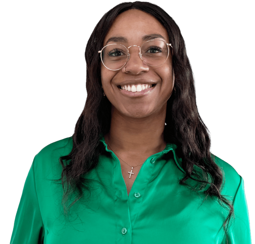 Sara Koppenhöfer, eine lächelnde Frau mit langen dunklen Haaren, die eine Brille, ein grünes Button-up-Hemd und eine Kreuzkette trägt, steht vor einem schlichten hellen Hintergrund.